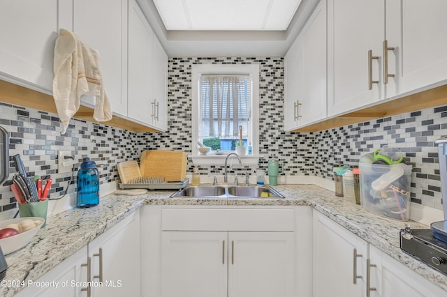 kitchen with backsplash, white cabinetry, and sink