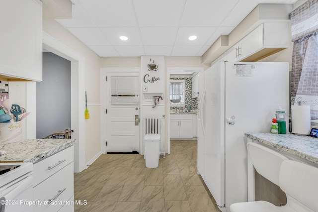 kitchen featuring white cabinets, white appliances, light stone counters, and a paneled ceiling