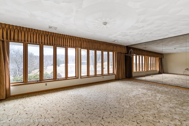 carpeted empty room featuring visible vents, baseboards, and a healthy amount of sunlight