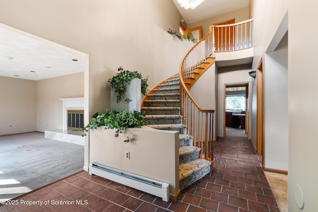 stairway with a baseboard radiator, carpet, a towering ceiling, and a fireplace