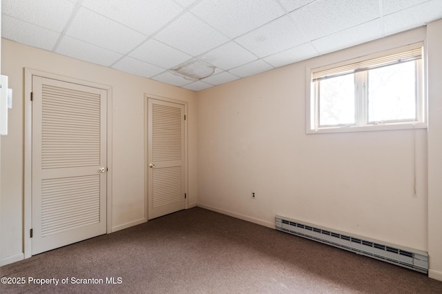 unfurnished bedroom featuring two closets, a baseboard heating unit, baseboards, carpet floors, and a paneled ceiling