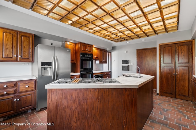 kitchen featuring an island with sink, light countertops, stainless steel fridge, dobule oven black, and a sink