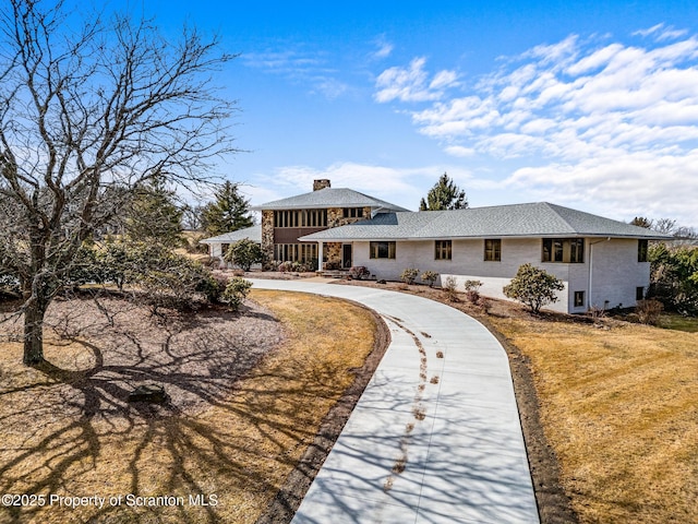 back of property featuring curved driveway, a chimney, and a yard