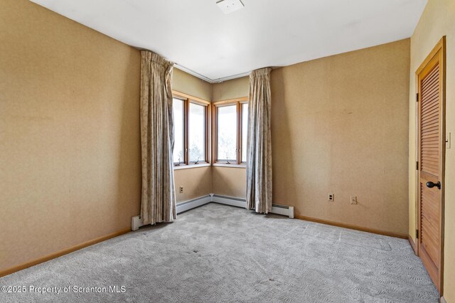 carpeted spare room featuring a baseboard heating unit and baseboards