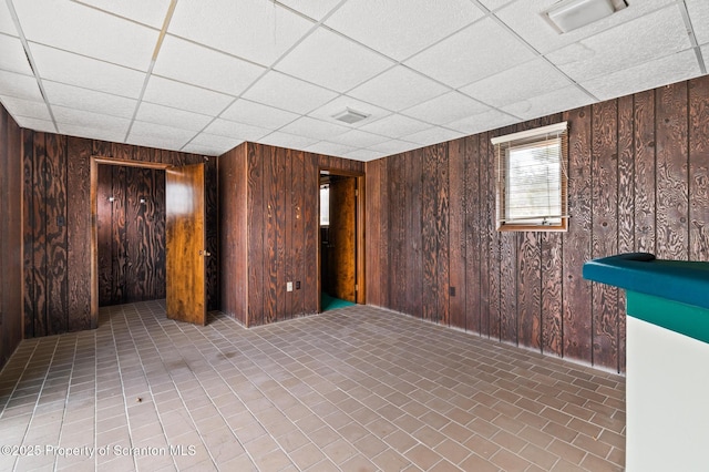 basement with wooden walls, a paneled ceiling, and visible vents