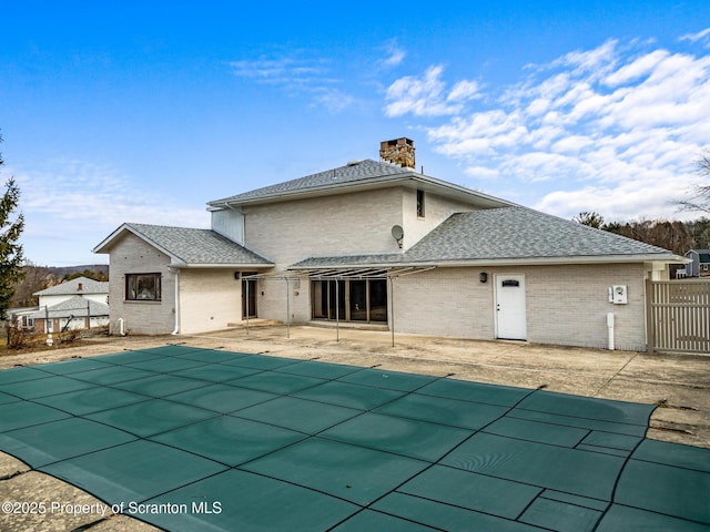 back of property with fence, a covered pool, a chimney, a patio area, and brick siding