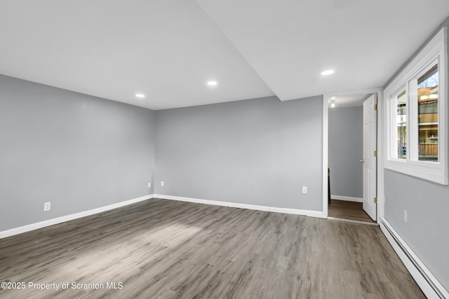 empty room featuring baseboards, a baseboard heating unit, wood finished floors, and recessed lighting