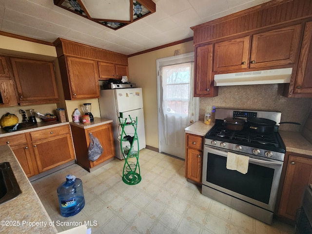 kitchen featuring brown cabinetry, light floors, freestanding refrigerator, under cabinet range hood, and stainless steel gas stove