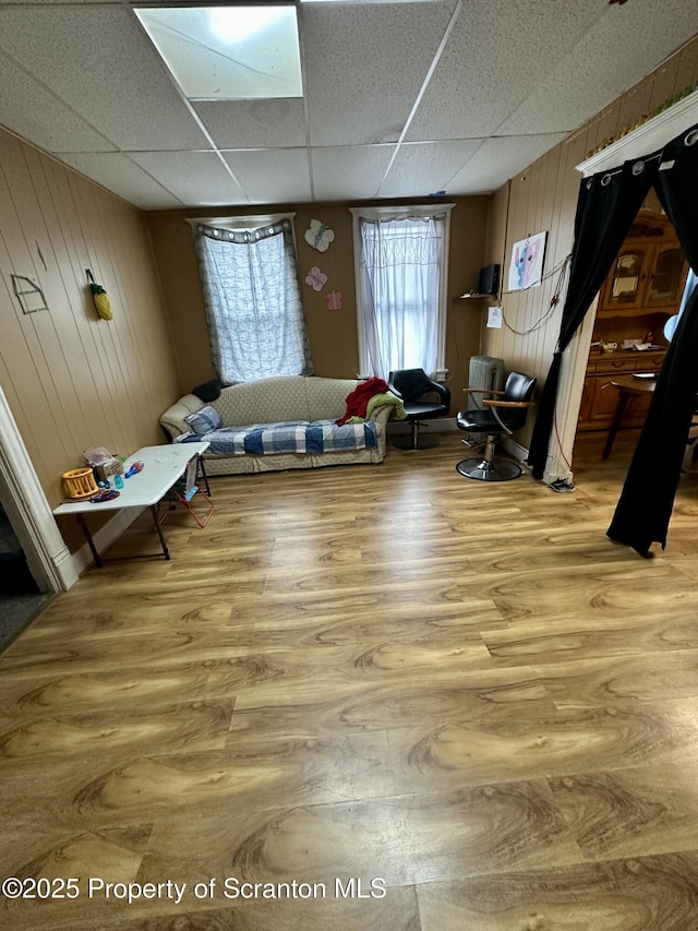 living area featuring wood walls, wood-type flooring, and a drop ceiling