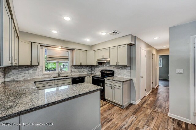 kitchen with black appliances, a sink, dark stone countertops, dark wood finished floors, and tasteful backsplash