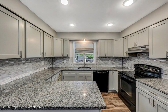 kitchen featuring black appliances, under cabinet range hood, a sink, wood finished floors, and stone counters