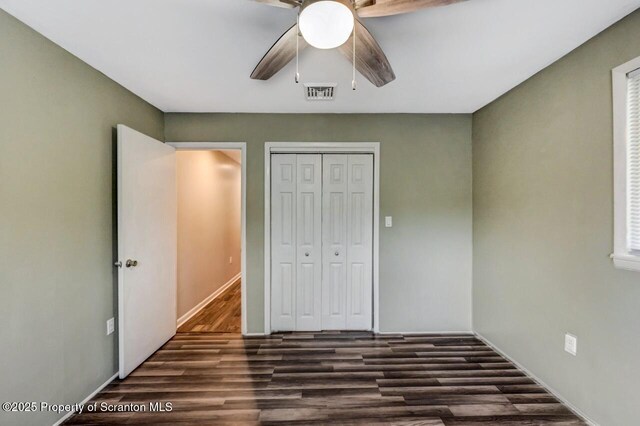 unfurnished bedroom with dark wood-style floors, a closet, a ceiling fan, and baseboards