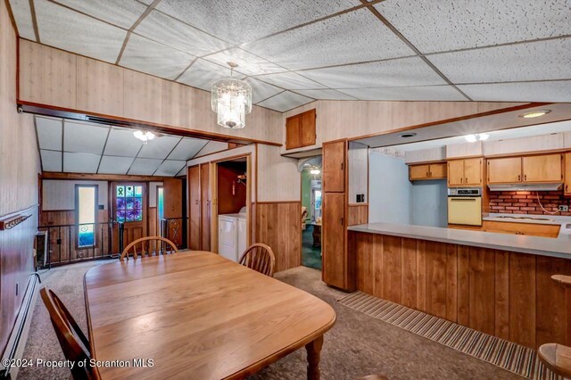 dining space with lofted ceiling, light carpet, a baseboard heating unit, wooden walls, and washer / dryer