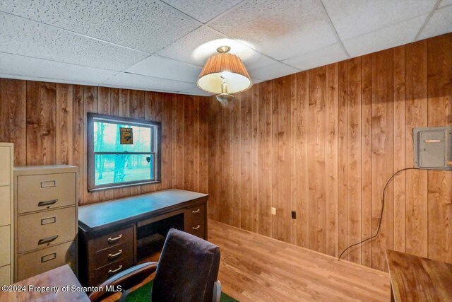 home office with electric panel, a drop ceiling, wooden walls, and hardwood / wood-style flooring