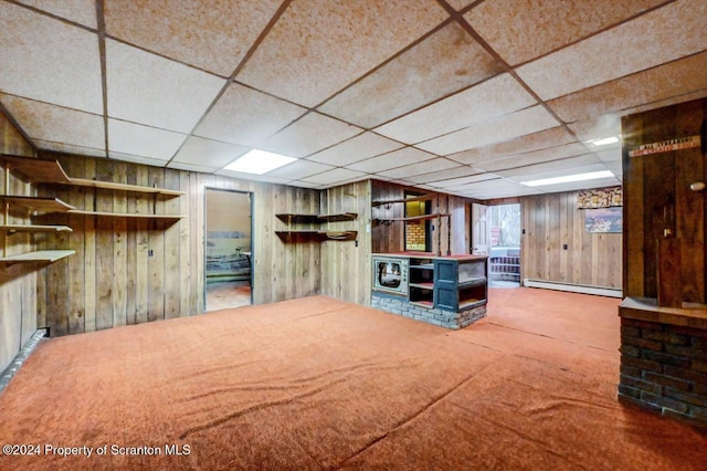 basement with a drop ceiling, carpet floors, baseboard heating, and wood walls