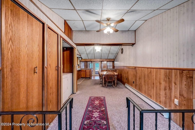 corridor with a paneled ceiling, light colored carpet, a baseboard radiator, and wood walls