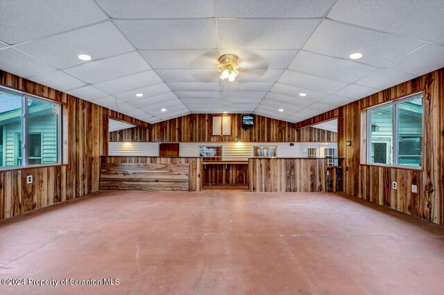 interior space with ceiling fan, wood walls, concrete floors, and vaulted ceiling