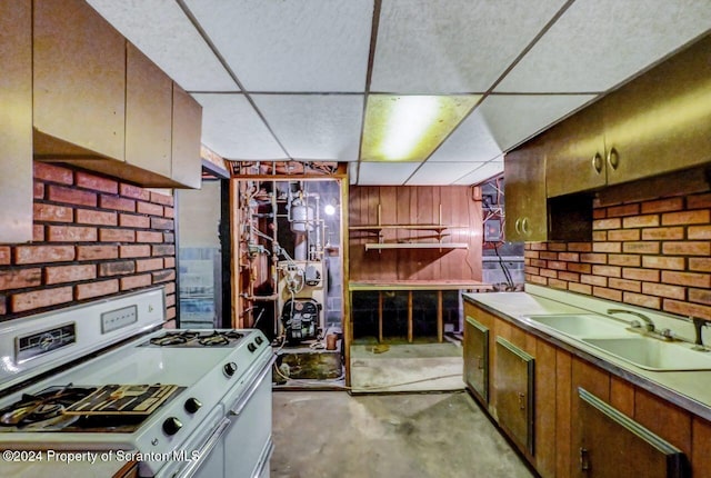 kitchen featuring concrete flooring, a drop ceiling, white range with gas cooktop, and sink