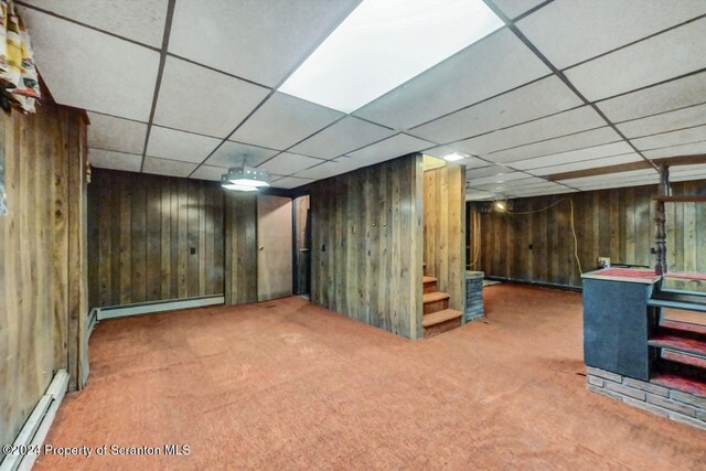 basement featuring carpet flooring, wooden walls, a drop ceiling, and a baseboard radiator