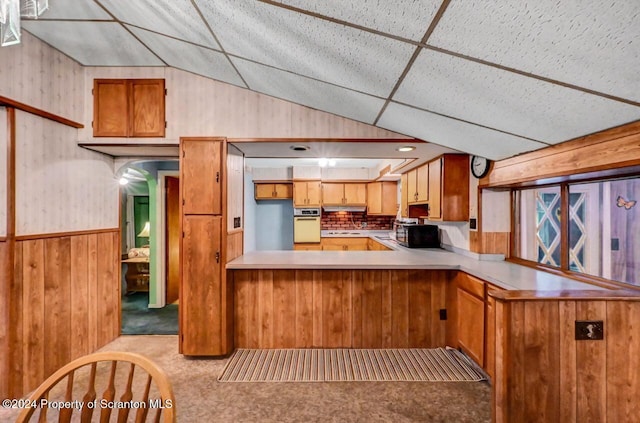 kitchen with kitchen peninsula, light carpet, oven, and wooden walls