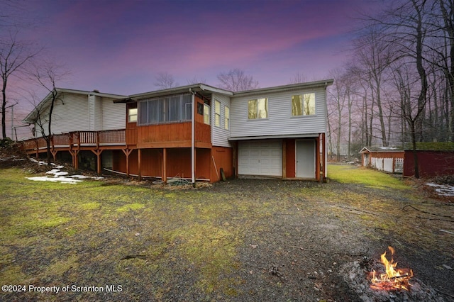 back house at dusk with a garage, a storage shed, and a deck