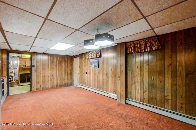 basement with carpet floors, a baseboard radiator, a drop ceiling, and wooden walls