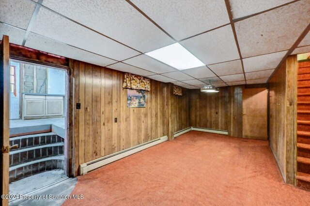 basement featuring carpet flooring, a drop ceiling, baseboard heating, and wooden walls