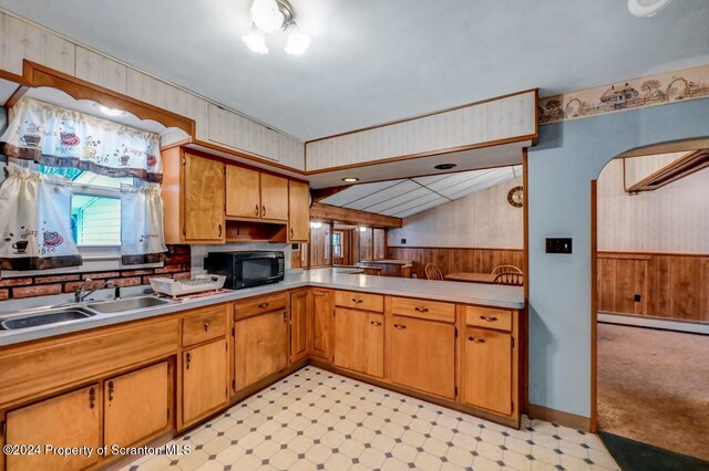 kitchen with kitchen peninsula, wood walls, baseboard heating, and sink