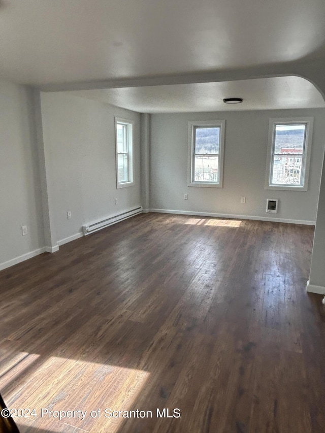 spare room featuring baseboard heating and dark hardwood / wood-style flooring