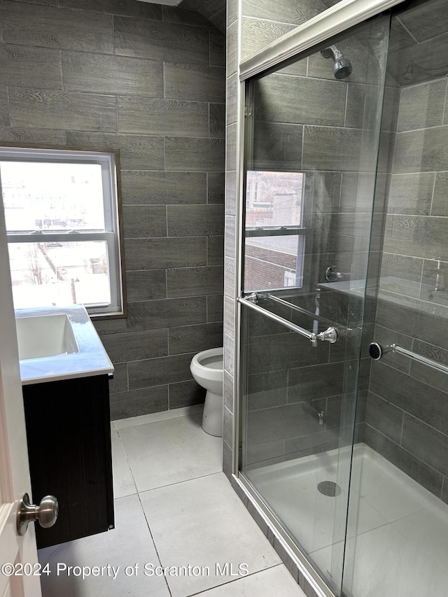 bathroom featuring tile patterned floors, an enclosed shower, toilet, vanity, and tile walls