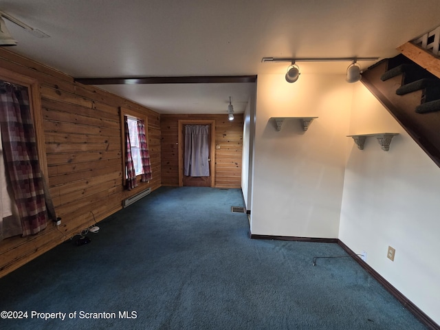 unfurnished living room featuring wood walls, dark colored carpet, rail lighting, and a baseboard heating unit