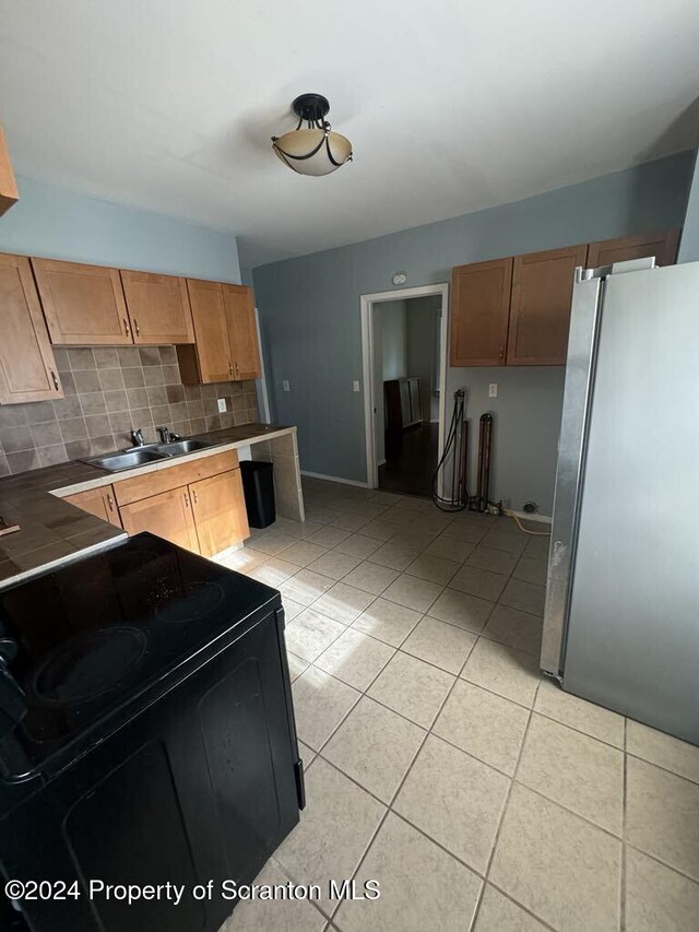 kitchen with black electric range, tile countertops, stainless steel fridge, decorative backsplash, and light tile patterned floors