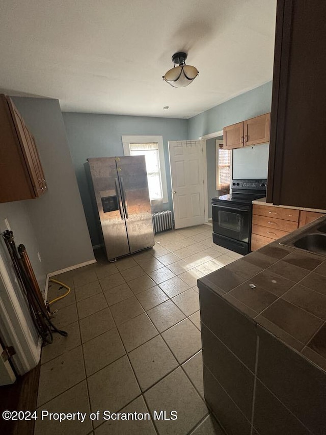 kitchen with tile countertops, radiator, sink, stainless steel fridge, and black / electric stove