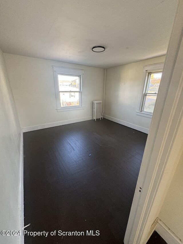 empty room featuring dark hardwood / wood-style floors, plenty of natural light, and radiator