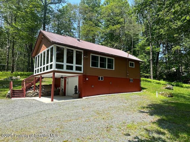 105 Hughes Dr, Greene Twp, PA 18426 - rustic home featuring a sunroom, stairway, a patio area, a metal roof, and view of scattered trees