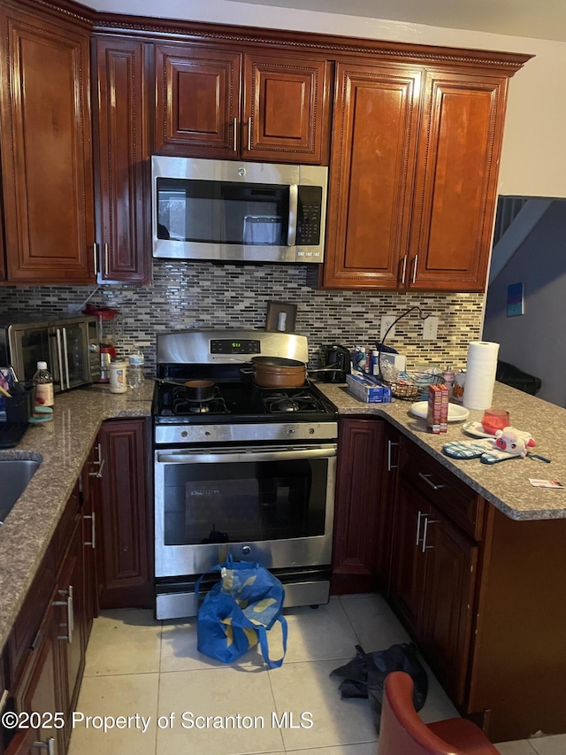 kitchen with appliances with stainless steel finishes, light tile patterned floors, light stone counters, and decorative backsplash