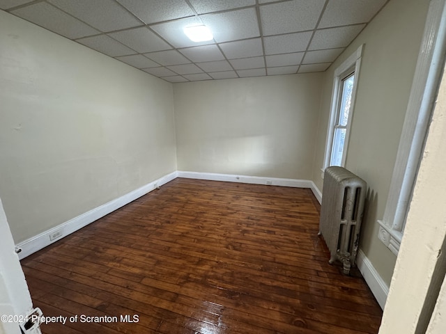 unfurnished room featuring a drop ceiling, dark hardwood / wood-style floors, and radiator