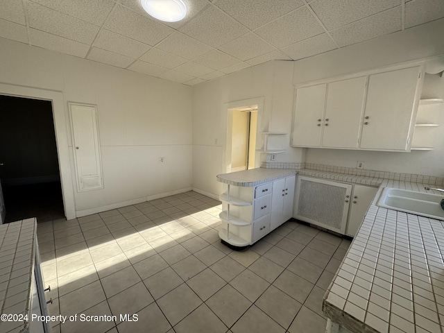 kitchen with light tile patterned floors, white cabinetry, tile counters, and sink