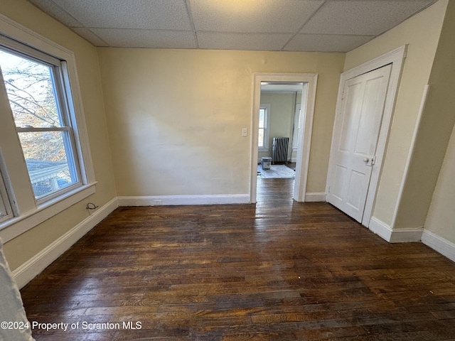 unfurnished room featuring radiator, a drop ceiling, and dark wood-type flooring