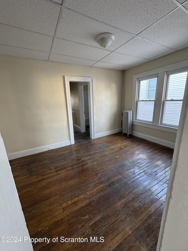 empty room with a paneled ceiling, radiator, and dark wood-type flooring