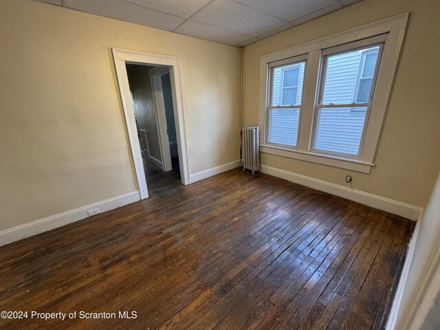 unfurnished room with radiator, a paneled ceiling, and dark hardwood / wood-style flooring