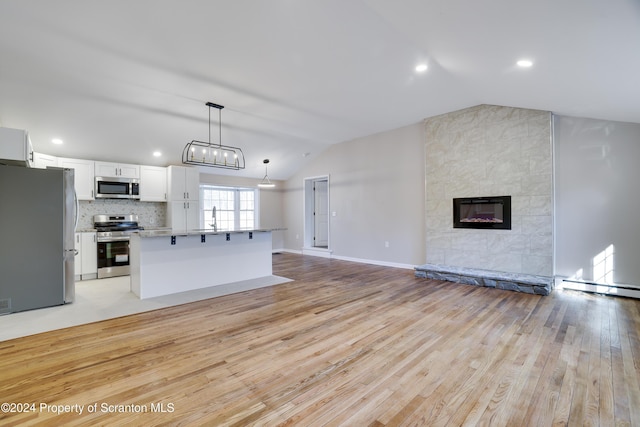 kitchen with white cabinetry, pendant lighting, lofted ceiling, a fireplace, and appliances with stainless steel finishes