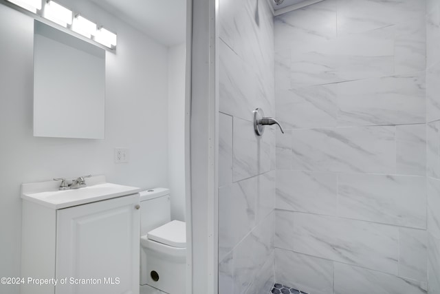 bathroom featuring a tile shower, vanity, and toilet