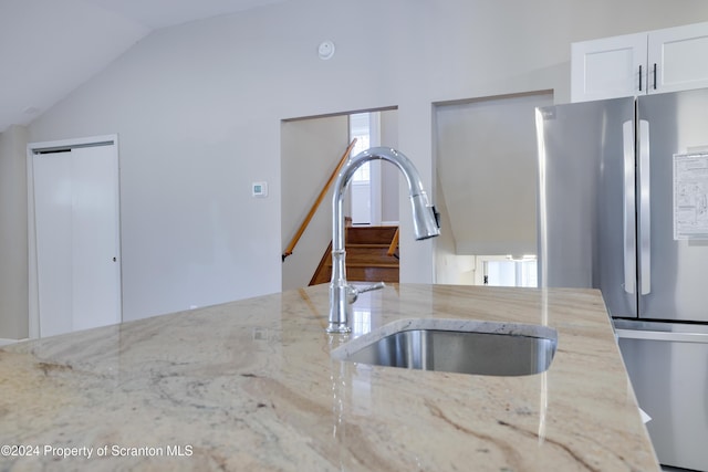 kitchen featuring sink, light stone counters, stainless steel fridge, lofted ceiling, and white cabinets