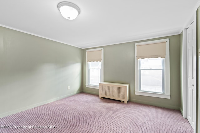 empty room featuring radiator heating unit, light colored carpet, and crown molding