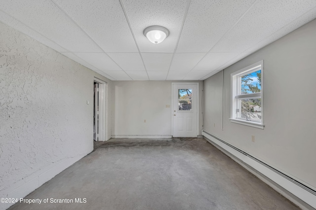 unfurnished room featuring concrete flooring, a paneled ceiling, and baseboard heating