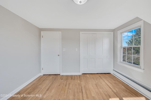 unfurnished bedroom featuring a closet, light wood-type flooring, and a baseboard heating unit