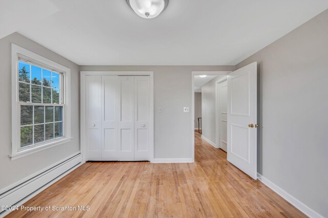 unfurnished bedroom with light hardwood / wood-style flooring, a closet, and a baseboard heating unit