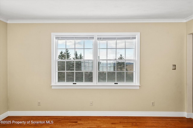 empty room with ornamental molding, baseboards, and wood finished floors