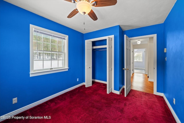 unfurnished bedroom featuring dark colored carpet, a closet, ceiling fan, and baseboards